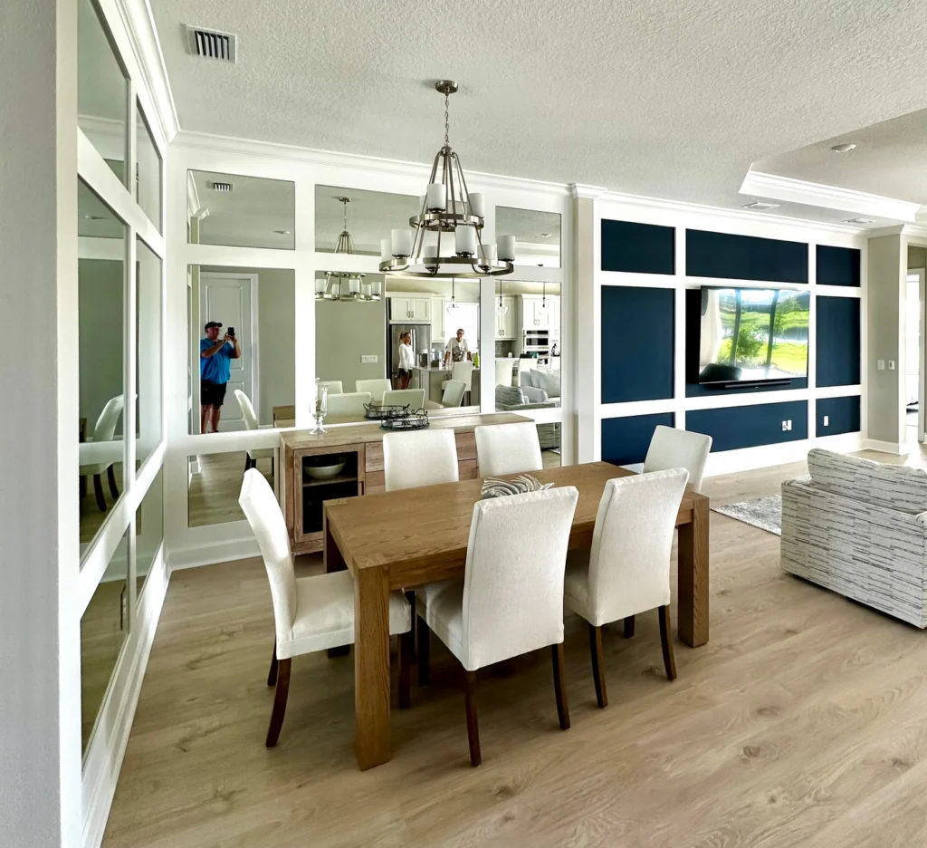 Dining table and sideboard reflected in a mirrored niche wall, with a navy-painted grid accent wall mounting a TV.
